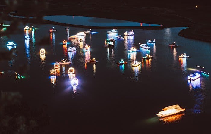Aerial view of a waterway filled with brightly lit boats, creating a colorful display against the dark water.