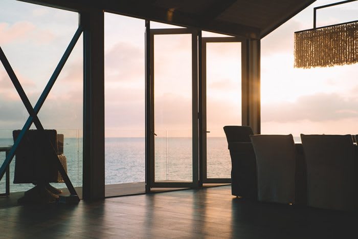 A modern interior with large glass doors opening to a serene ocean view at sunset, featuring stylish furniture.
