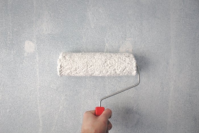 A hand holding a paint roller against a light blue wall, ready to apply paint.